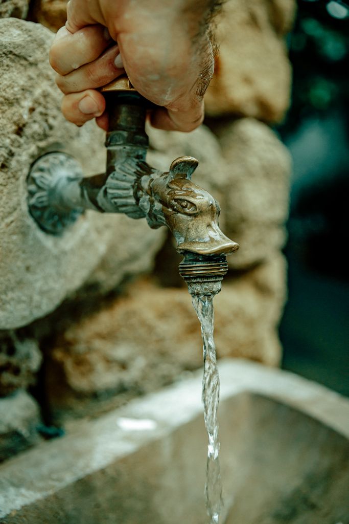 A vintage metal faucet with running water against a stone wall, depicting rustic charm.